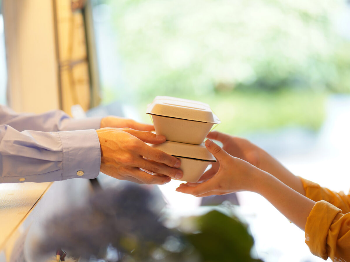 温かい料理の容器をカウンター越しに手渡す手元